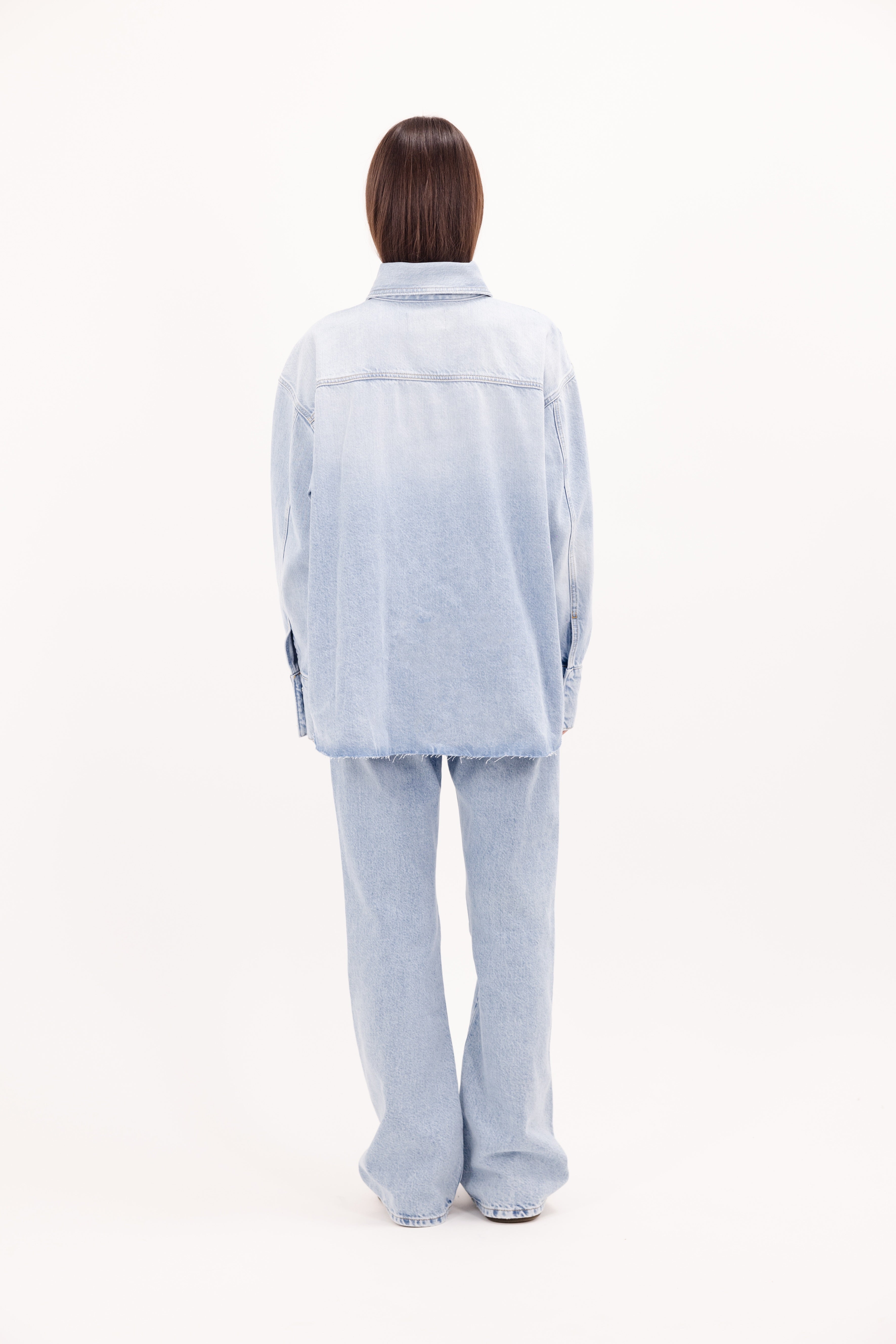 Back view of Mila women’s oversize shirt in bleached wash, 100% rigid cotton denim, worn by a model with jeans.