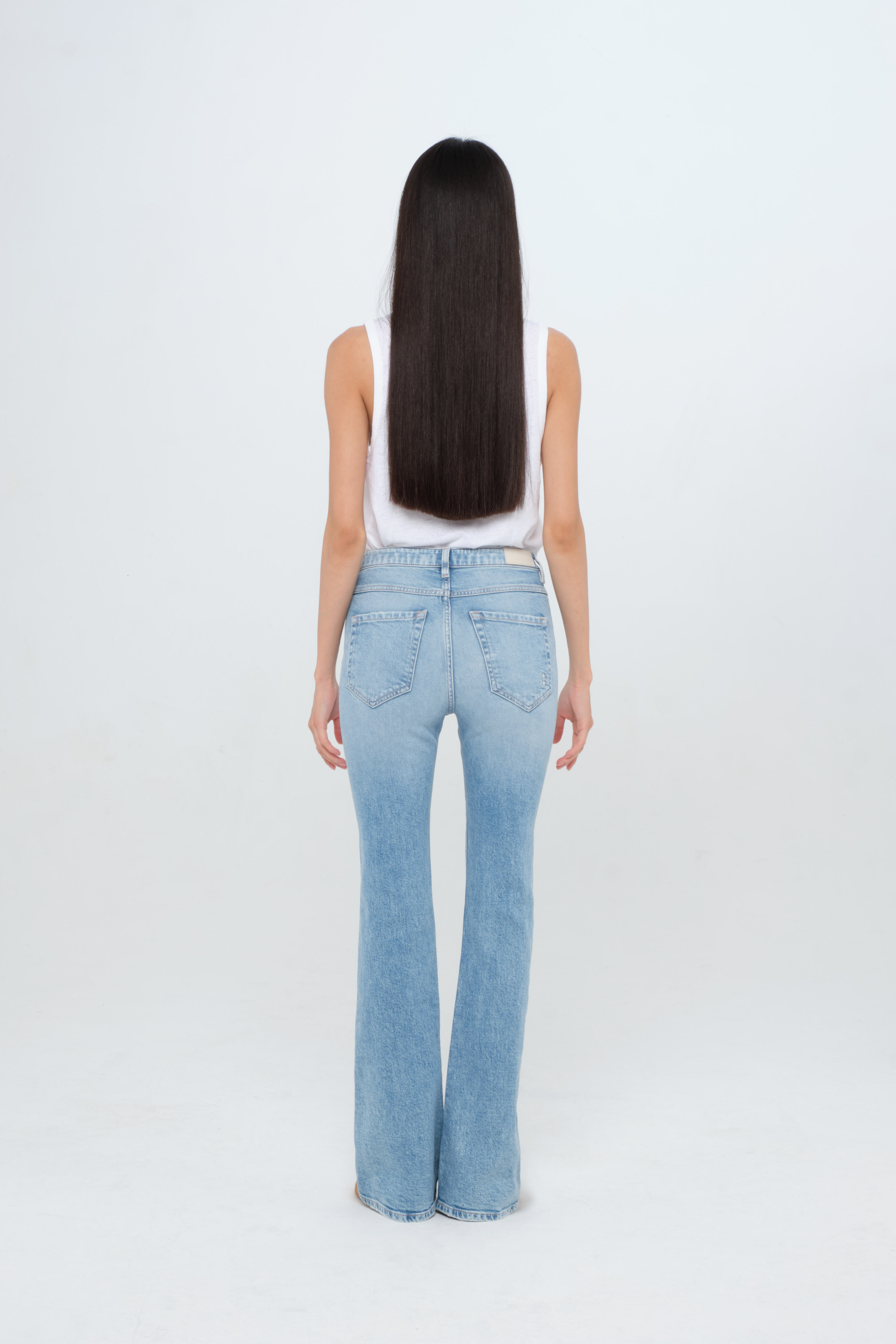 Back view of Natie women’s flared leg jeans in light wash, 99% cotton denim and 1% elastan fibers, worn by a model with a white t-shirt.