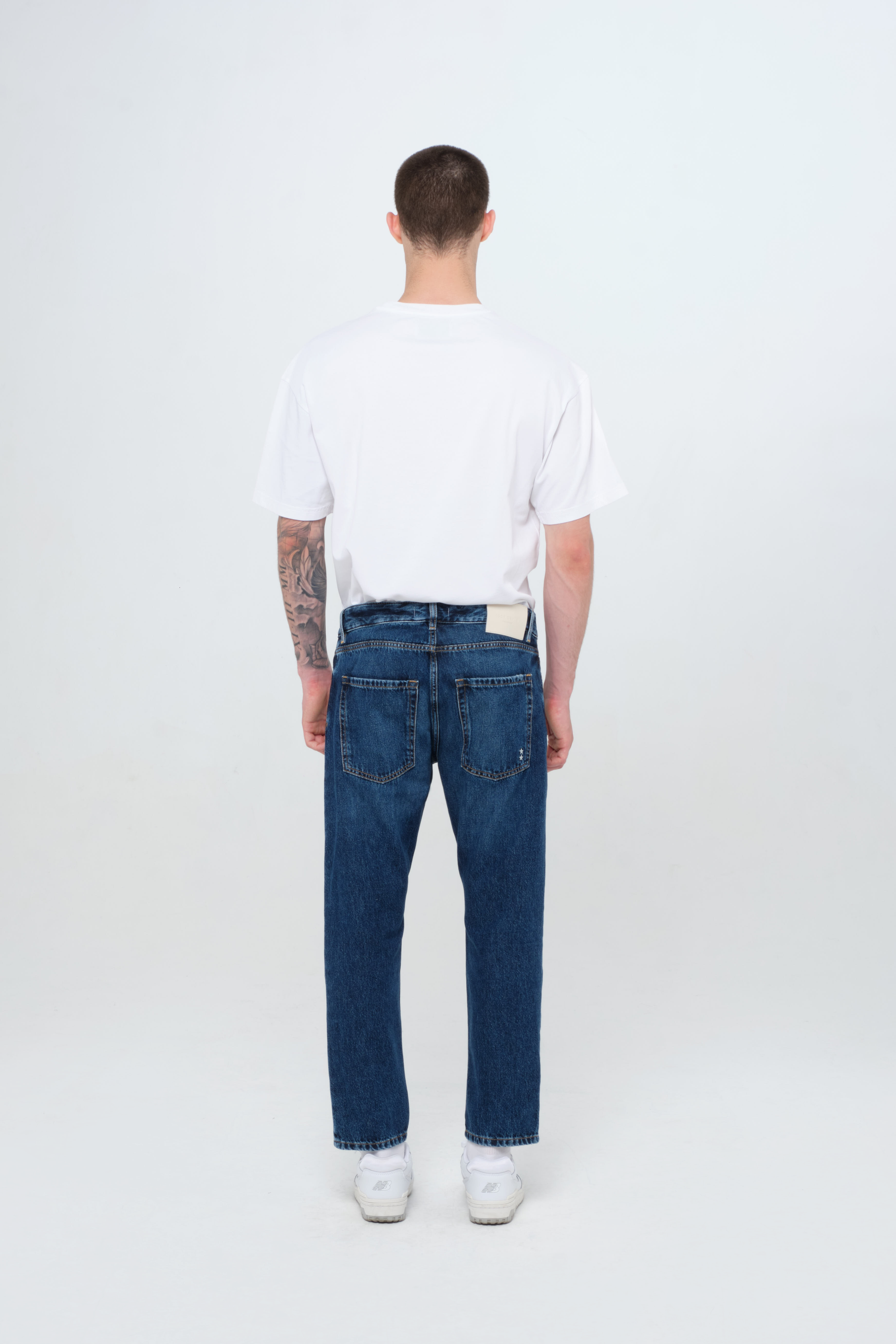 Back view of Nick men’s regular jeans in dark wash, 100% rigid cotton denim, worn by a model with a white t-shirt.
