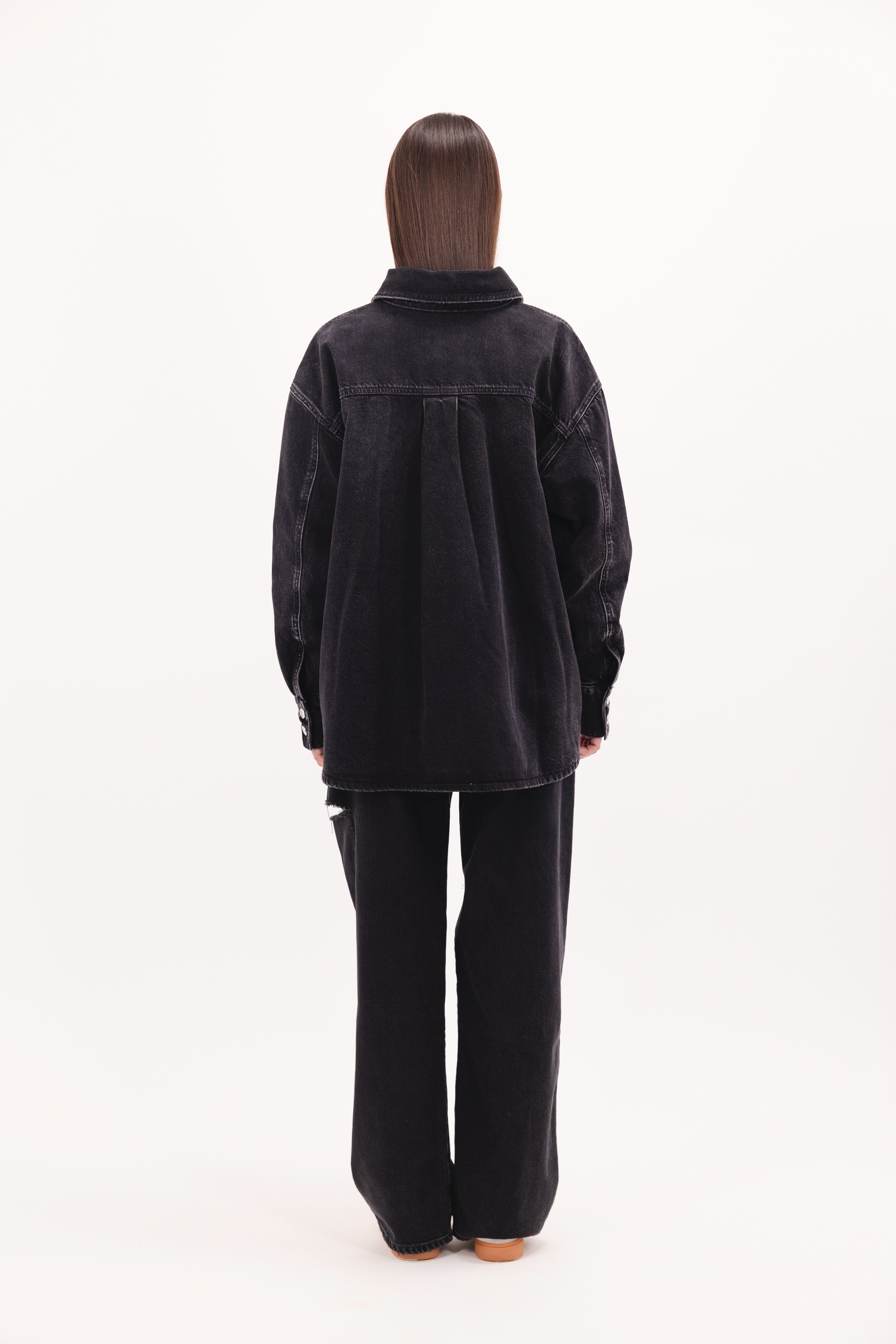 Back view of Noa women’s oversize shirt in graphite black wash, 100% rigid cotton denim, worn by a model with jeans.