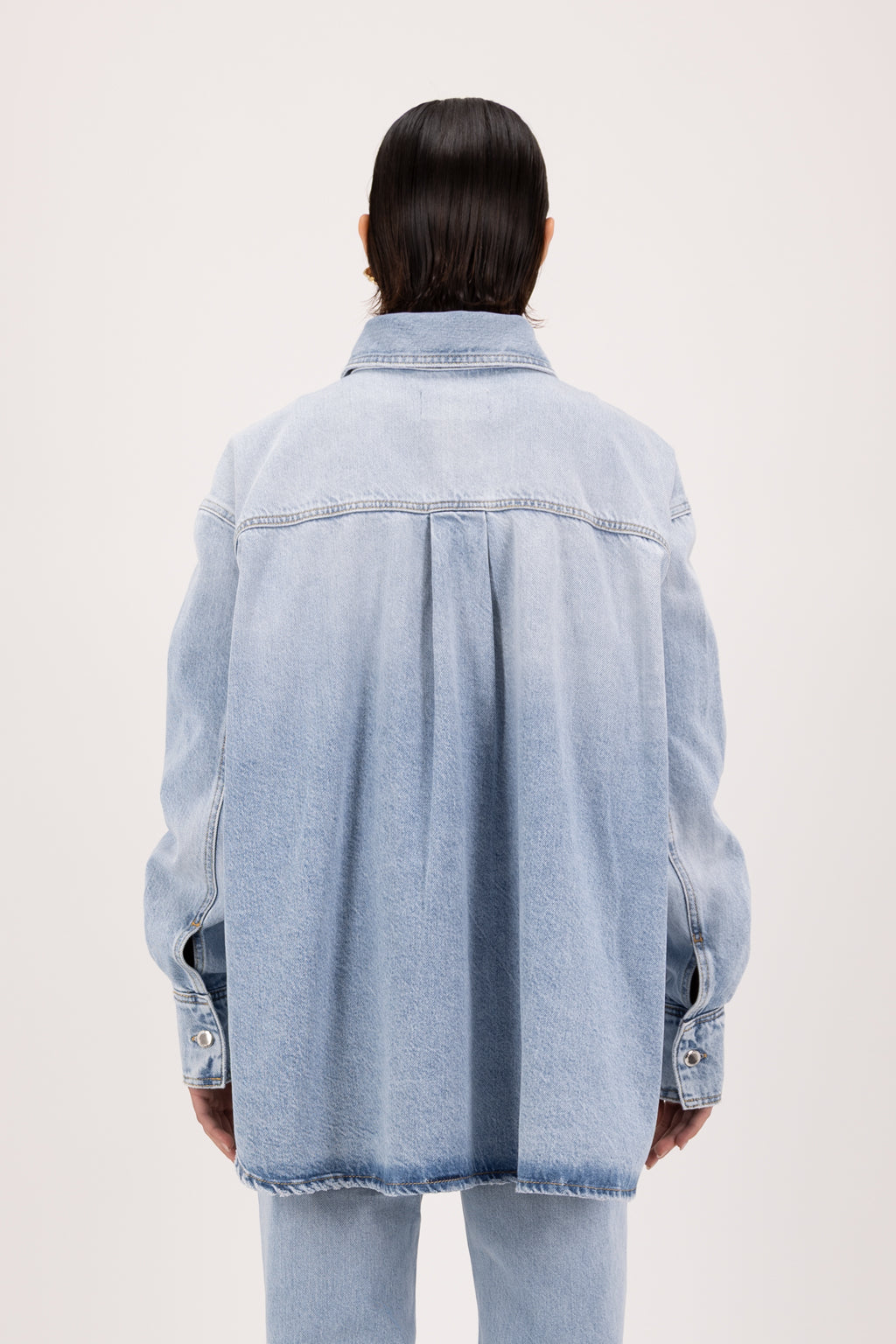Back view of Noa women’s oversize shirt in sky blue wash, 100% rigid cotton denim, worn by a model with jeans.