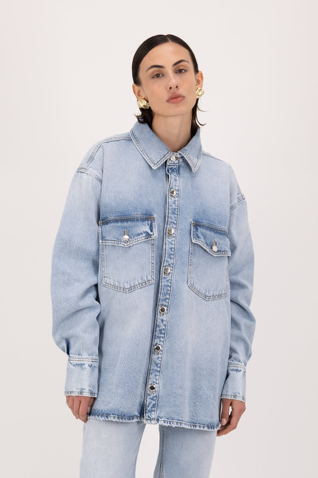 Noa women’s oversize shirt in sky blue wash, 100% rigid cotton denim, worn by a model with jeans.