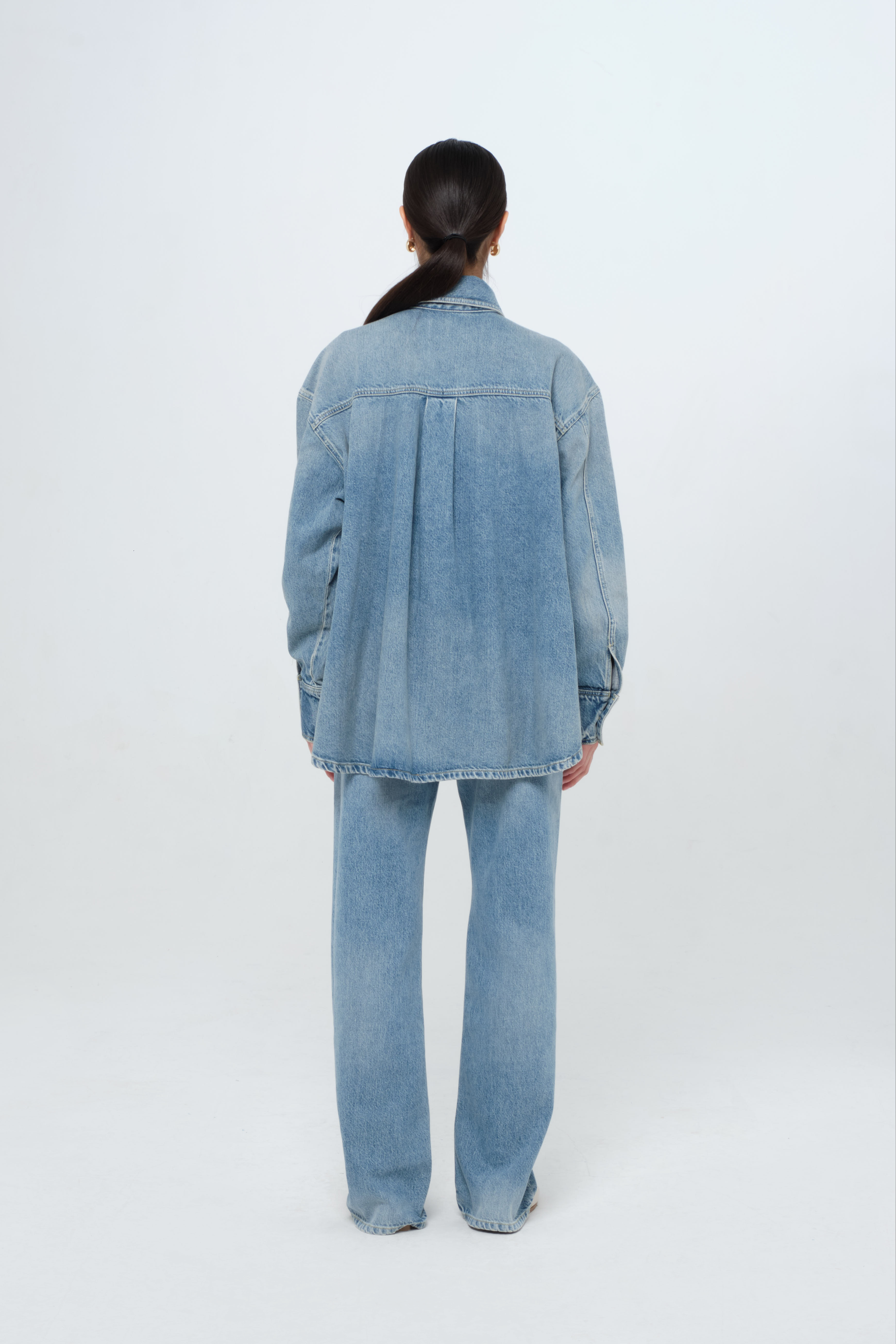 Back view of Noa women’s oversize shirt in smoke blue wash, 100% rigid cotton denim, worn by a model with jeans.