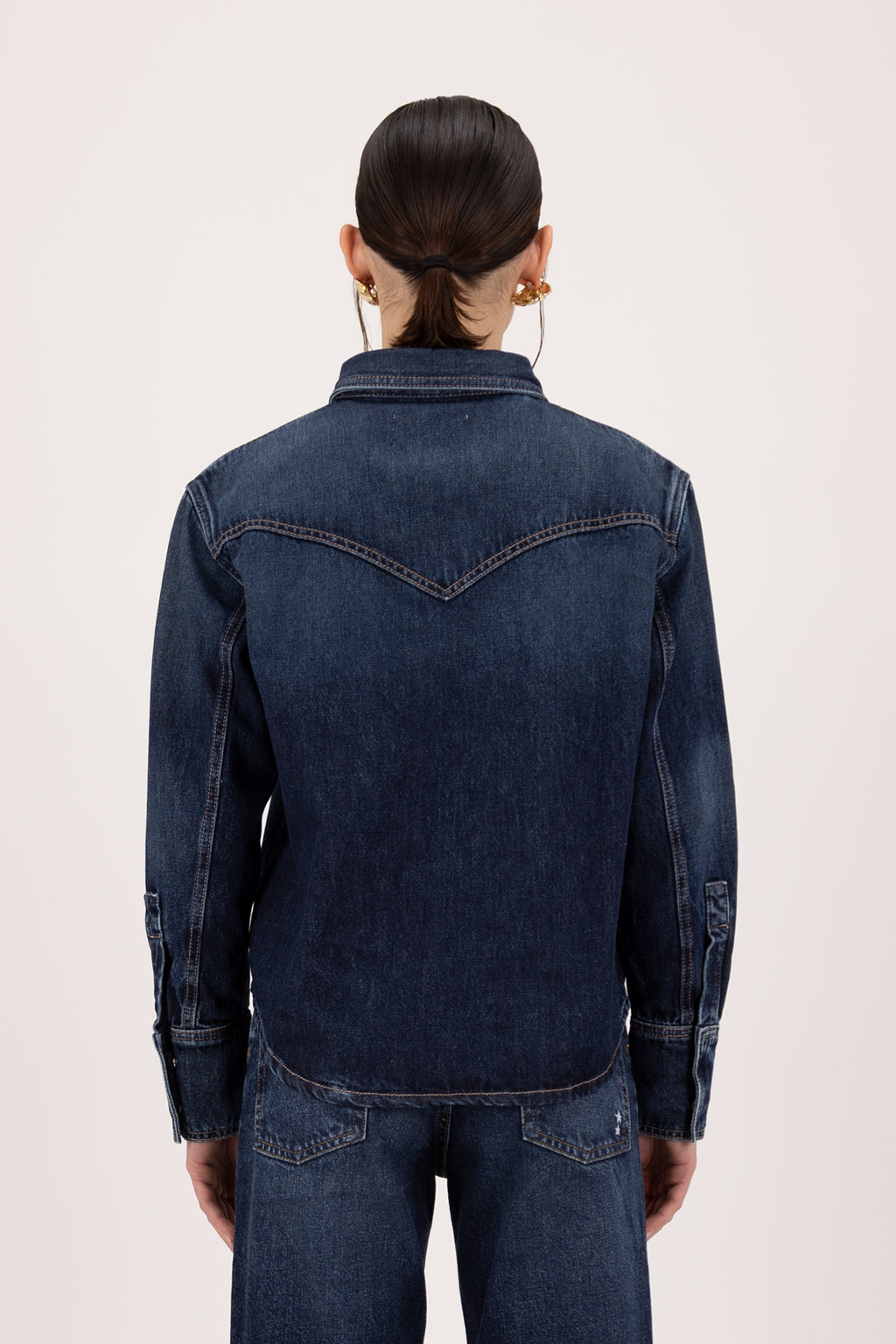 Back view of Norah women’s regular shirt in deep blue wash, 100% rigid soft cotton denim, worn by a model with jeans.