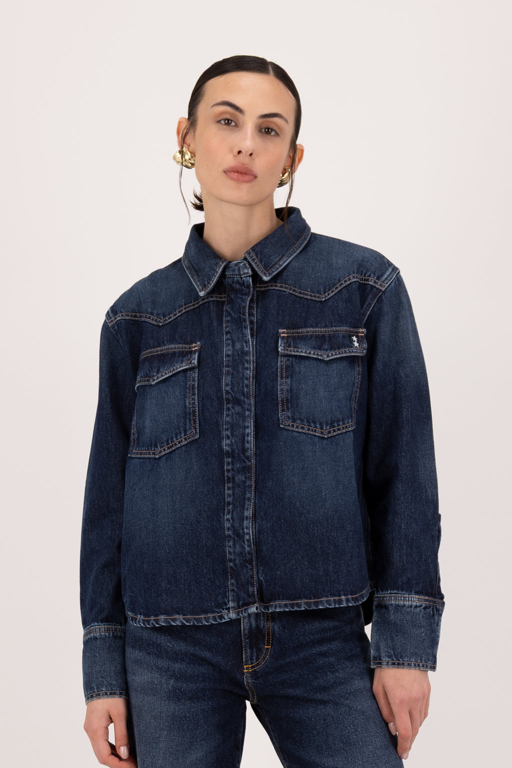 Norah women’s regular shirt in deep blue wash, 100% rigid soft cotton denim, worn by a model with jeans.