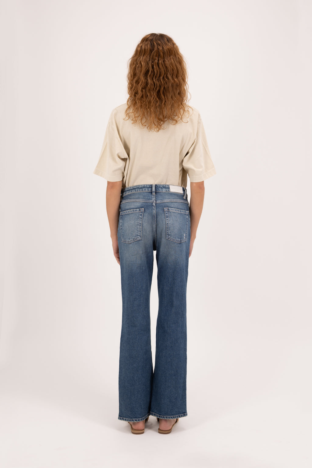 Back view of Pammy women’s slim flared jeans in dark used wash, 99% cotton denim and 1% Elastan fibers, worn by a model with a desert t-shirt.