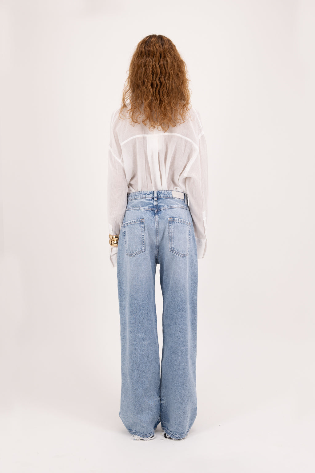 Back view of Poppy Eco women’s wide leg jeans in arid blue wash, 100% organic rigid cotton denim, worn by a model with a white shirt.