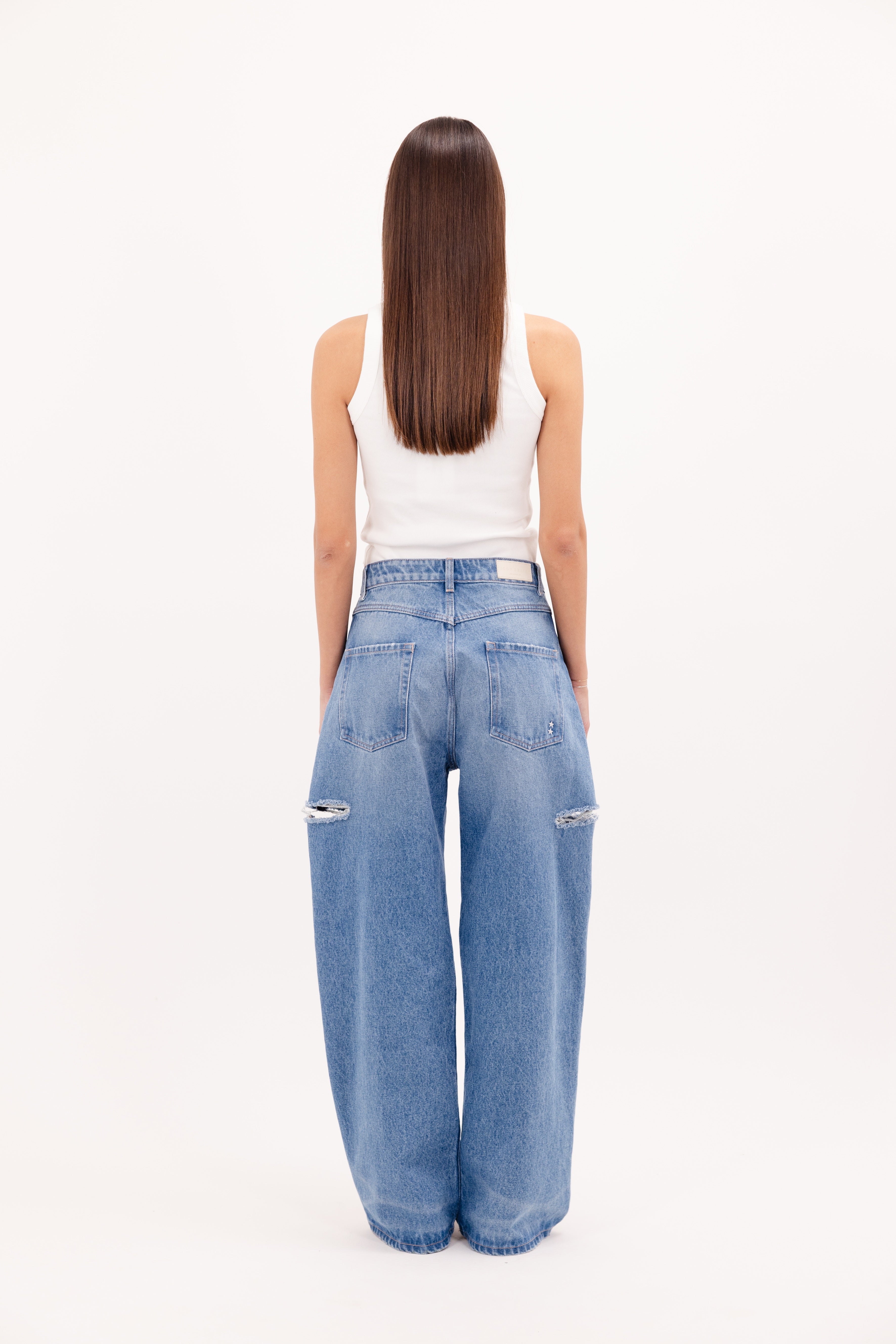 Back view of Poppy eco women’s wide leg jeans in deep ocean wash, 100% rigid organic cotton denim, worn by a model with a white tank top.