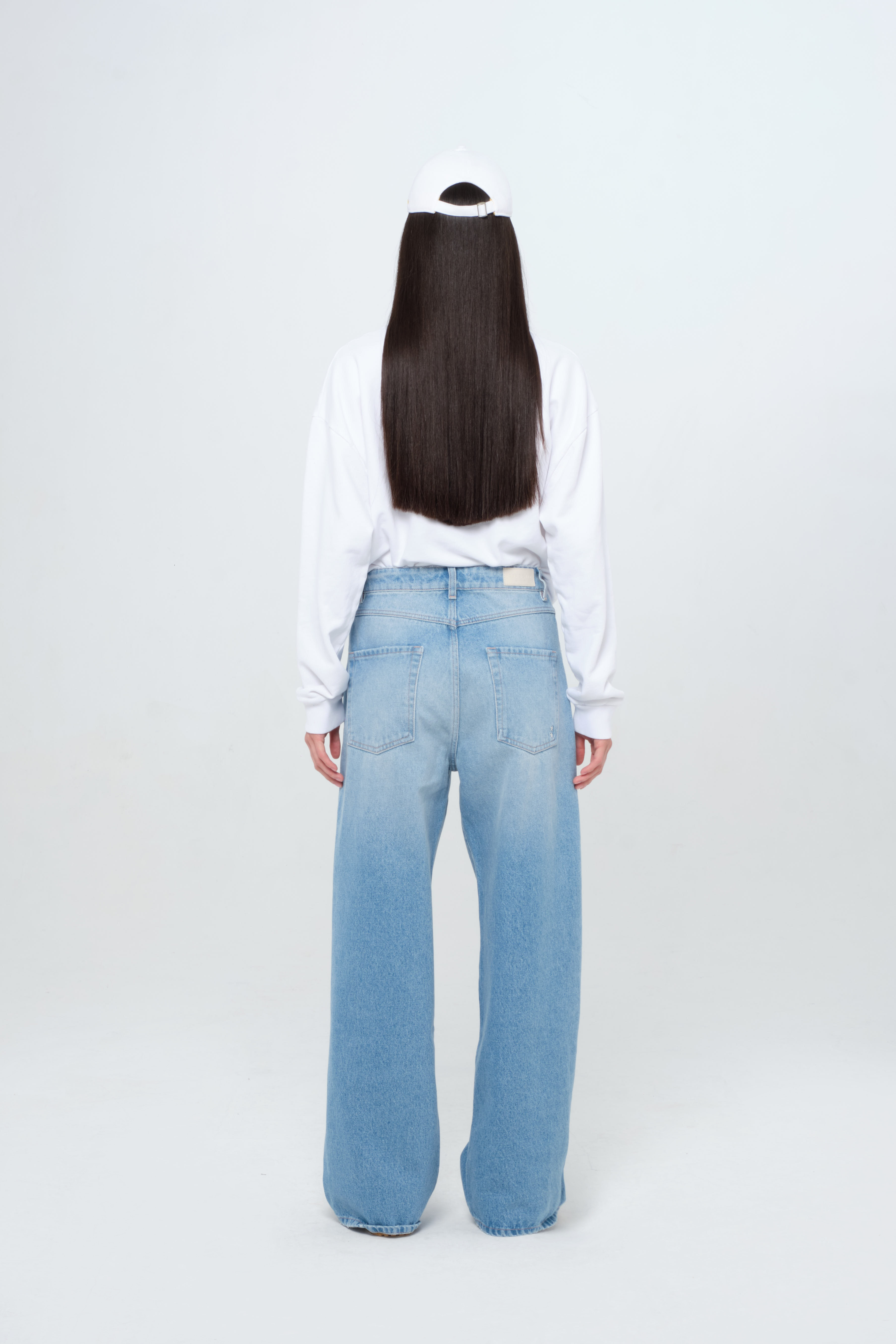 Back view of Poppy eco women’s wide leg jeans in medium wash, 100% rigid organic cotton denim, worn by a model with a white sweatshirt.
