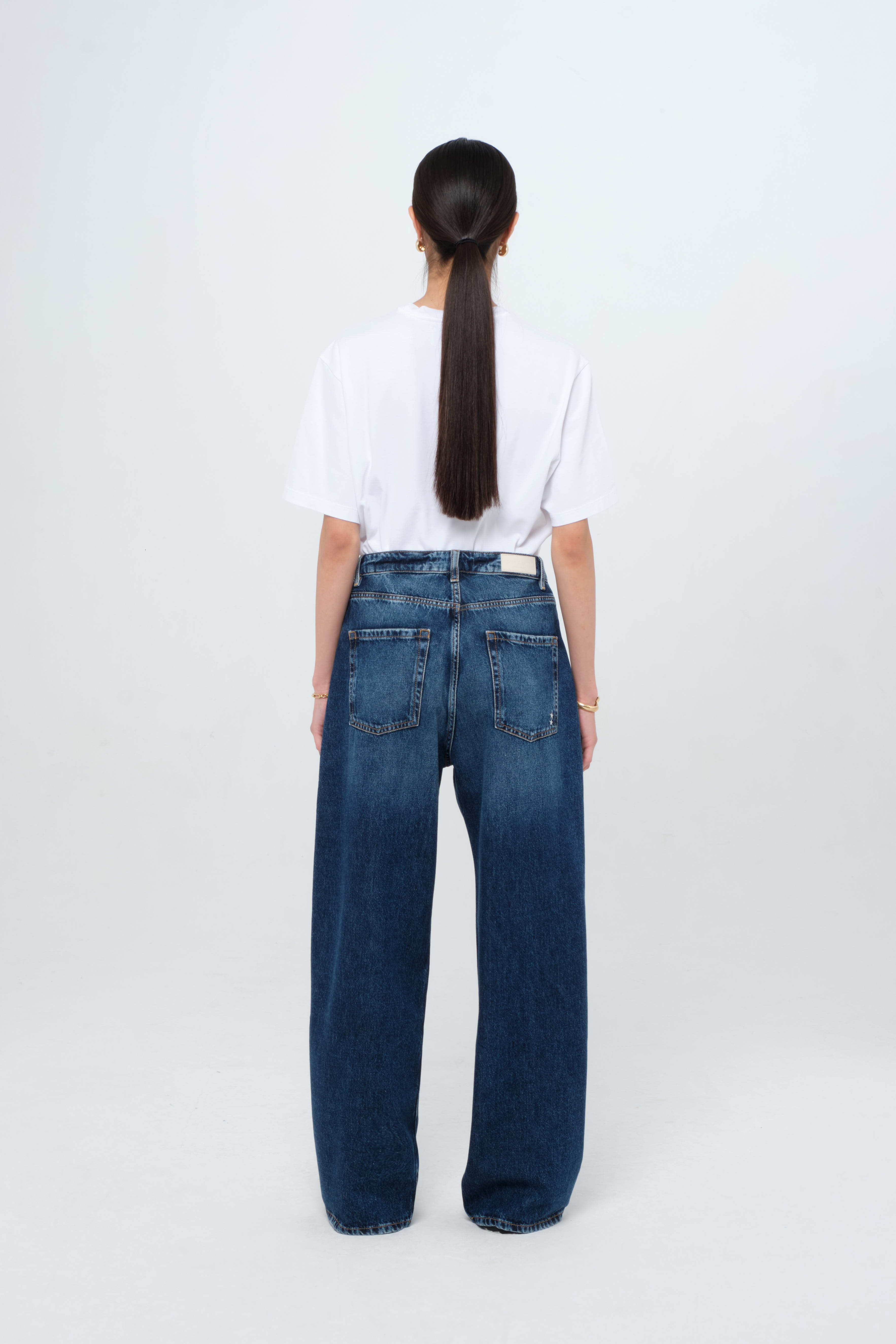 Back view of Poppy women’s wide leg jeans in dark wash, 100% rigid cotton denim, worn by a model with a white t-shirt.