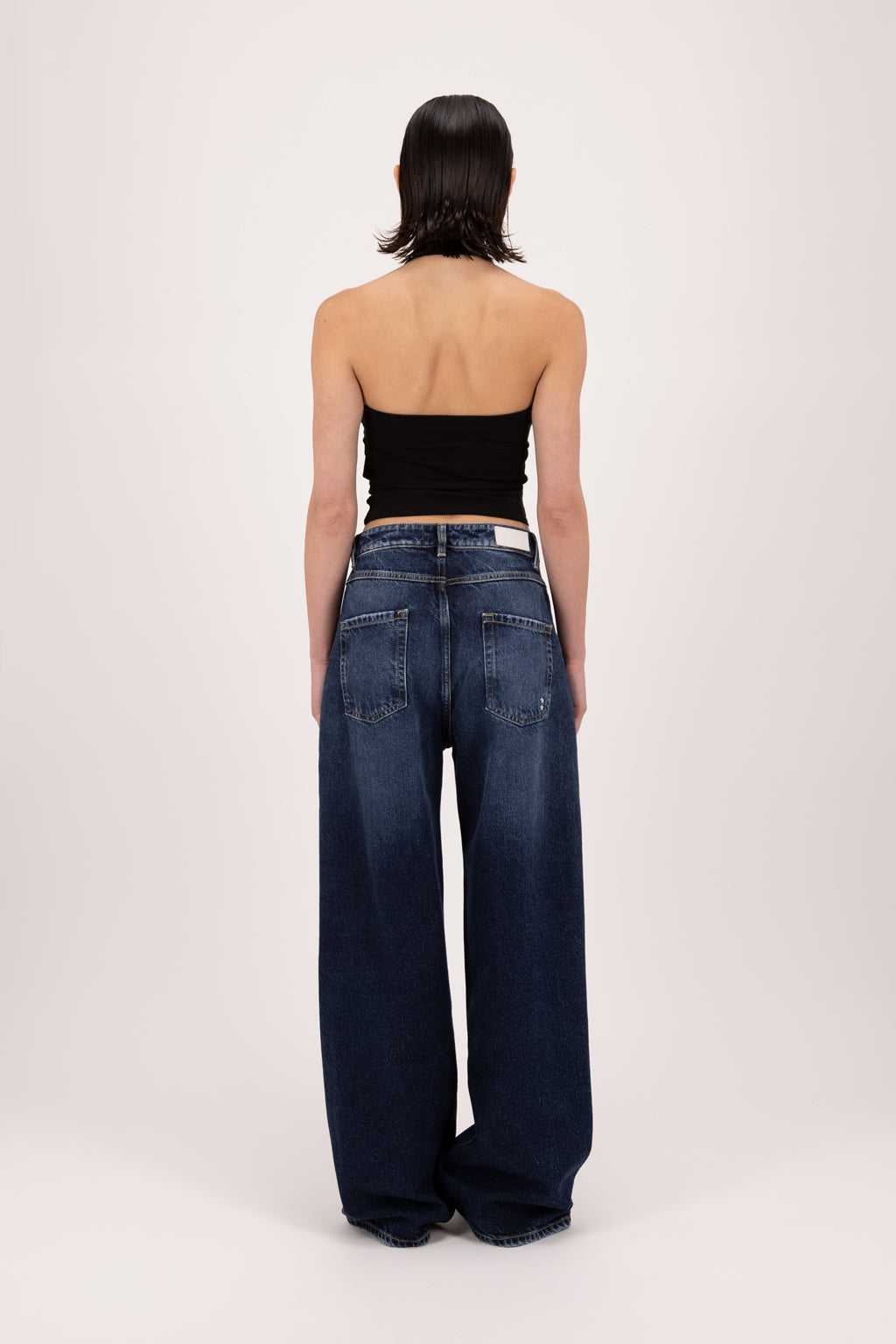 Back view of Poppy women’s wide leg jeans in deep blue wash, 100% rigid cotton denim, worn by a model with a black tank top.