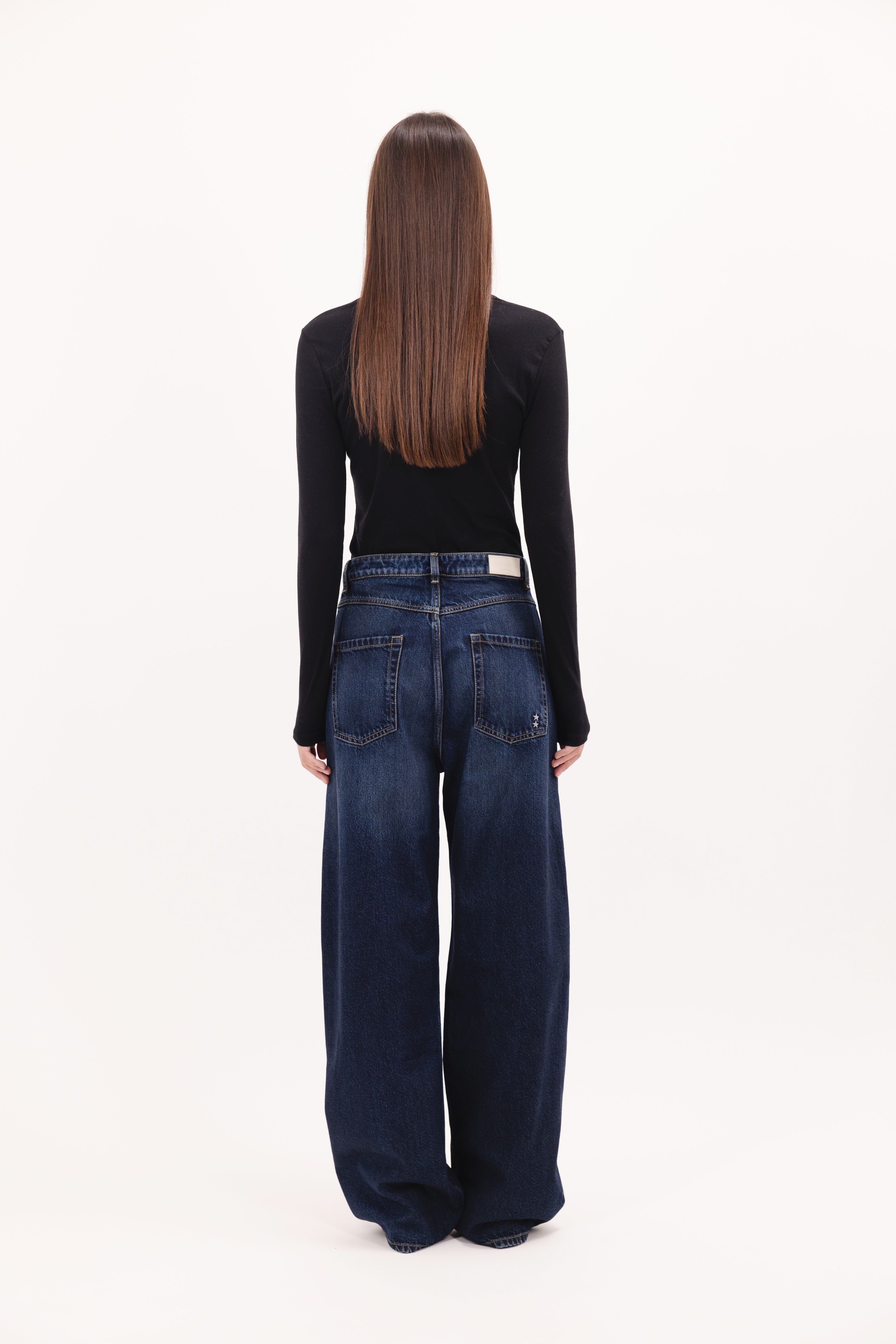Back view of Poppy women’s wide leg jeans in dusty blue wash, 100% rigid cotton denim, worn by a model with a black top.