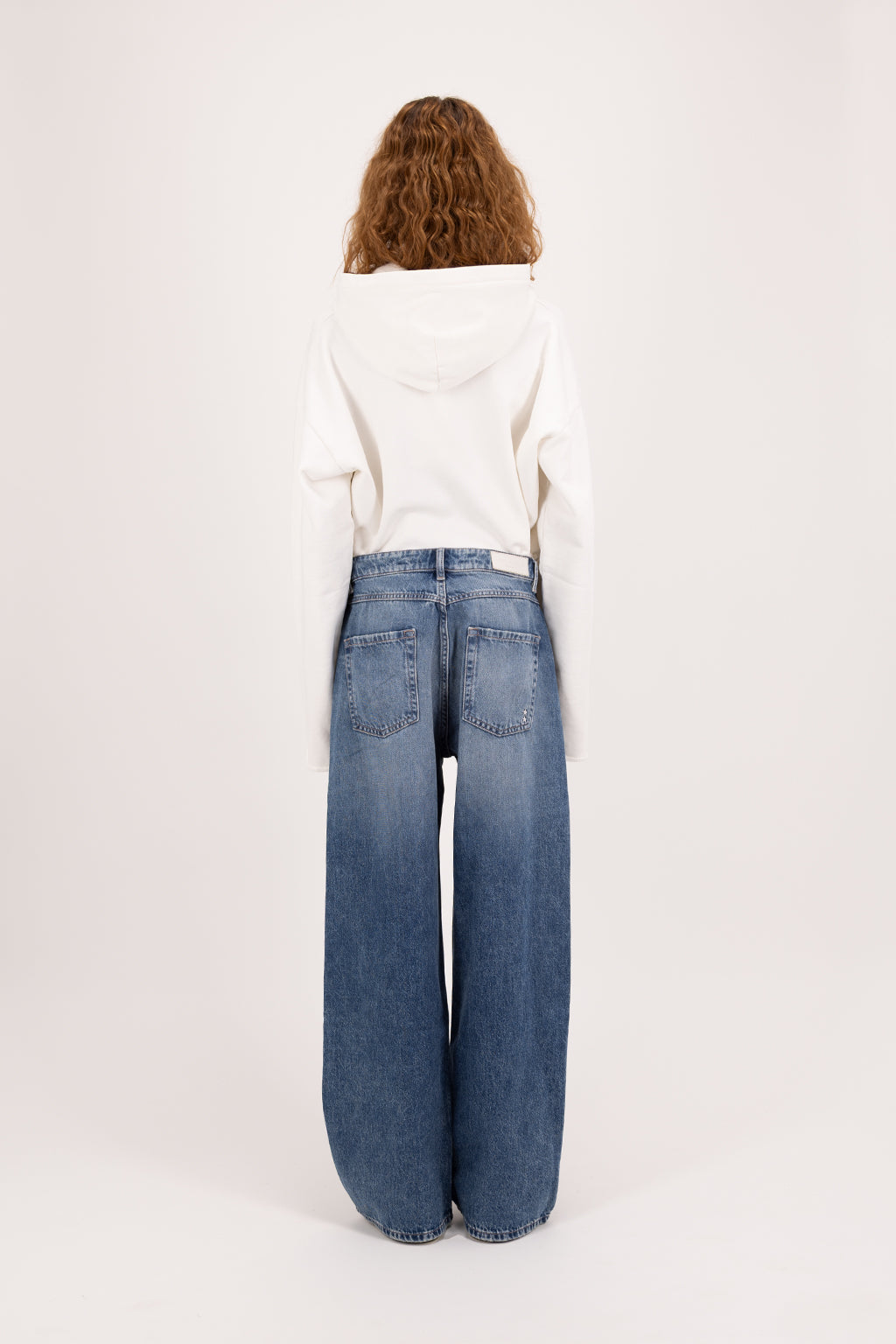 Back view of Poppy women’s wide leg jeans in deep blue wash, 100% rigid cotton denim, worn by a model with a black tank top.