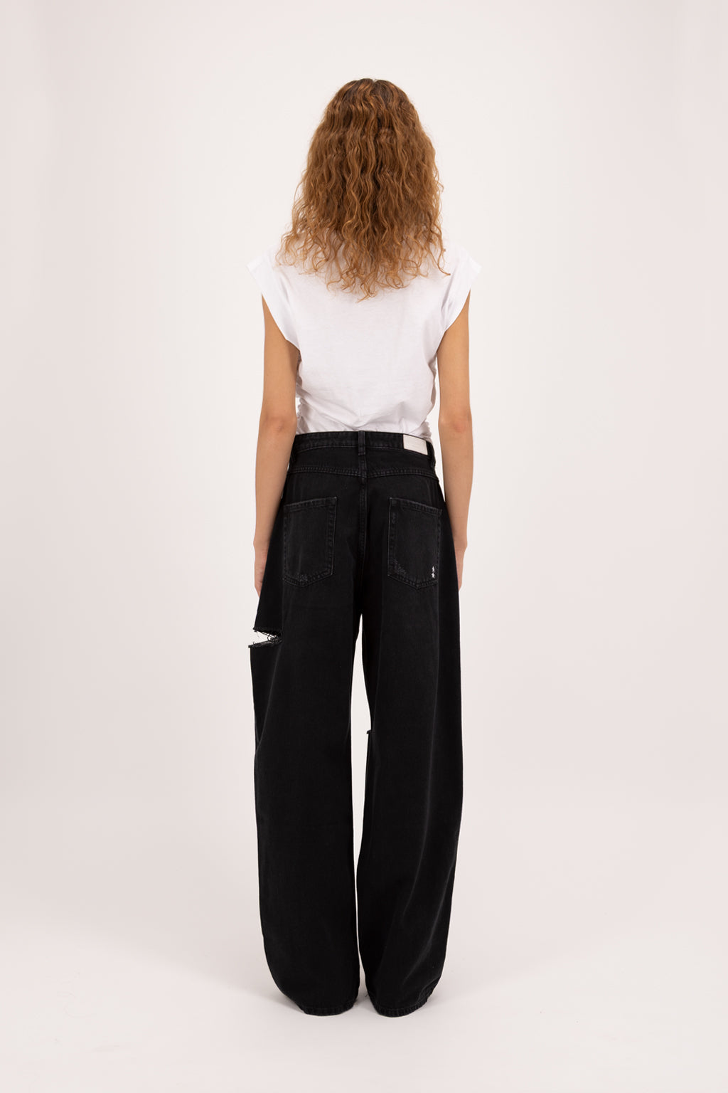 Back view of Poppy women’s wide leg jeans in graphite black wash, 100% rigid soft cotton denim, worn by a model with a white t-shirt.