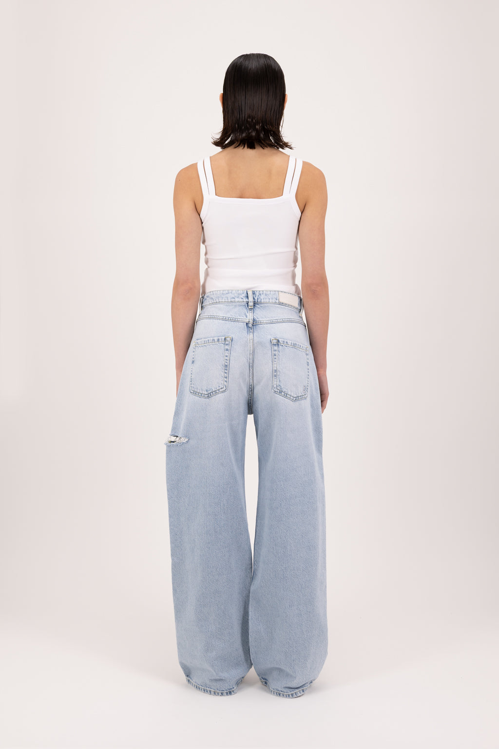 Back view of Poppy women’s wide leg jeans in sky blue wash, 100% rigid cotton denim, worn by a model with a white top.