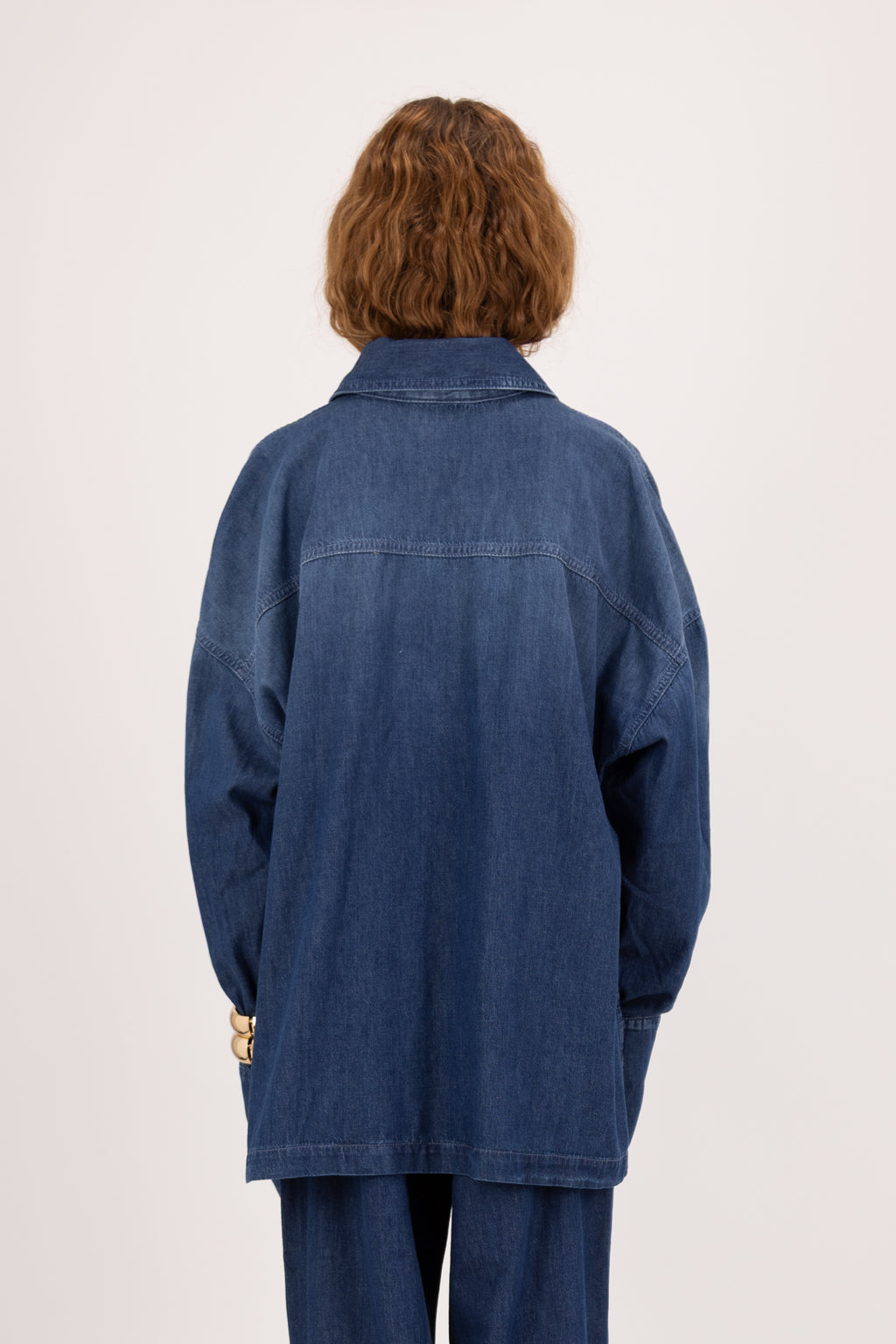 Back view of Rena women’s oversize shirt in night wash, 100% ultra light cotton denim, worn by a model with jeans.