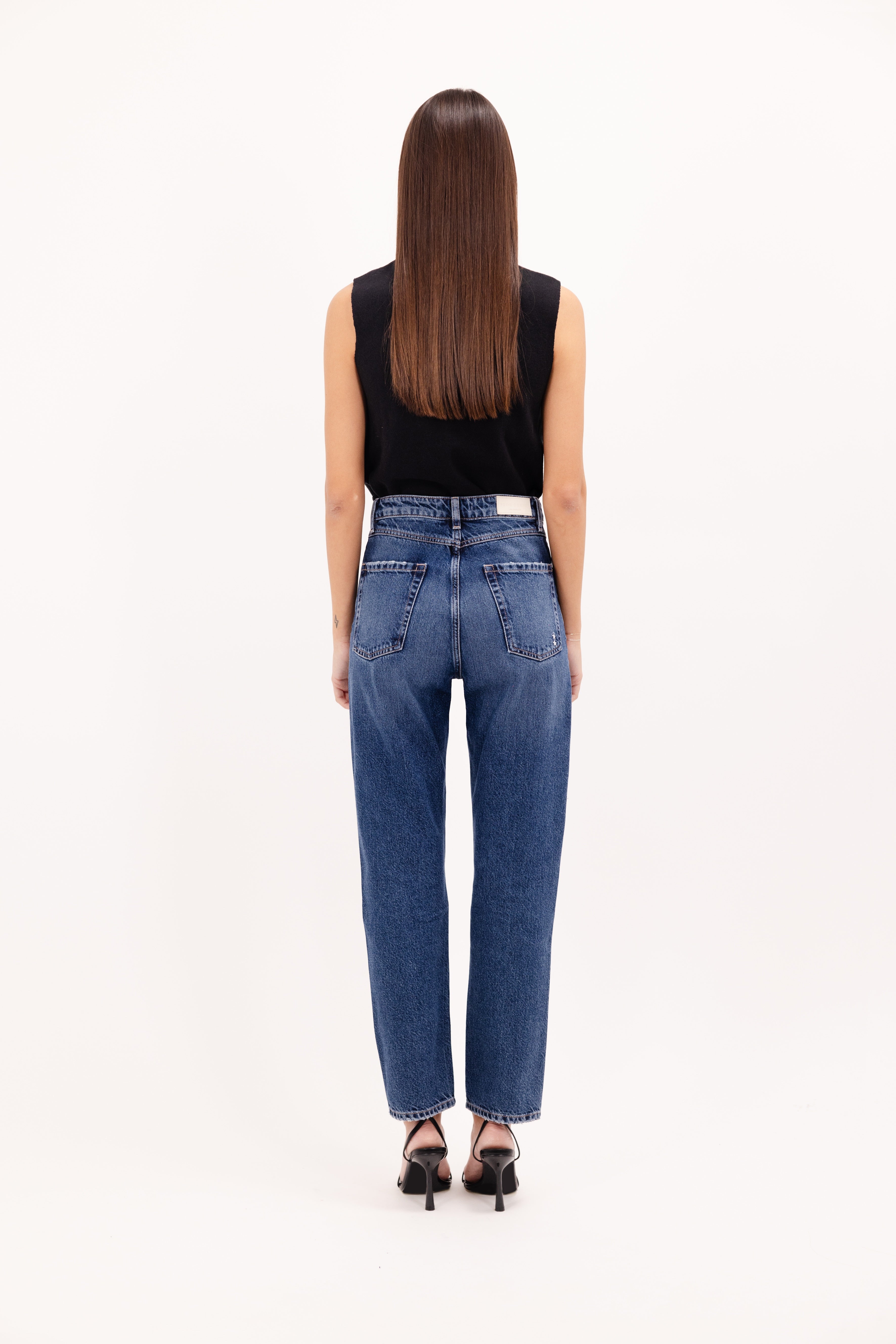 Back view of Rory women’s loose jeans in eclipse wash, 100% rigid cotton denim, worn by a model with a black top.