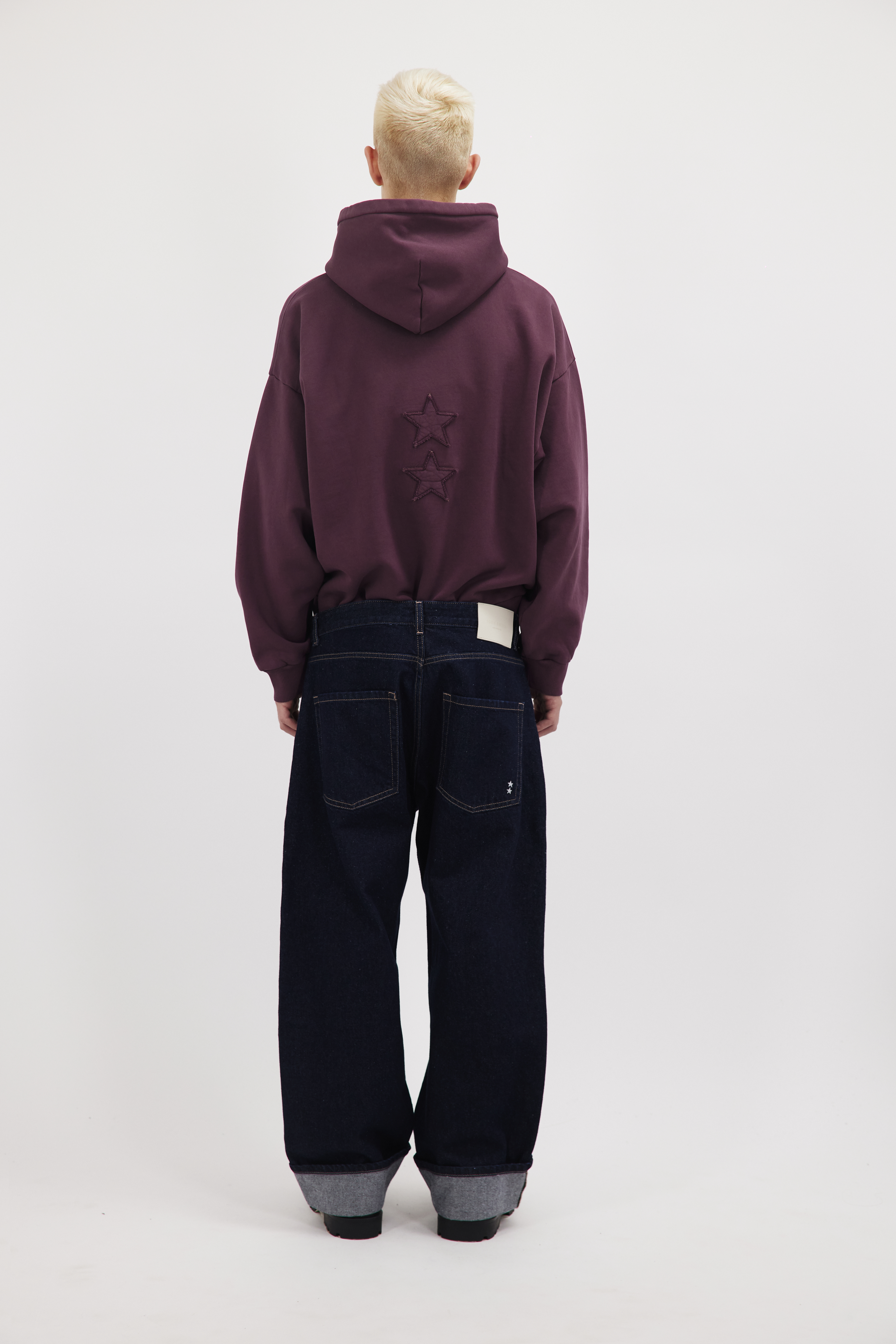 Back view of Will men’s wide leg baggy jeans in indigo raw wash, 100% rigid cotton denim, worn by a model with a cherry sweatshirt.