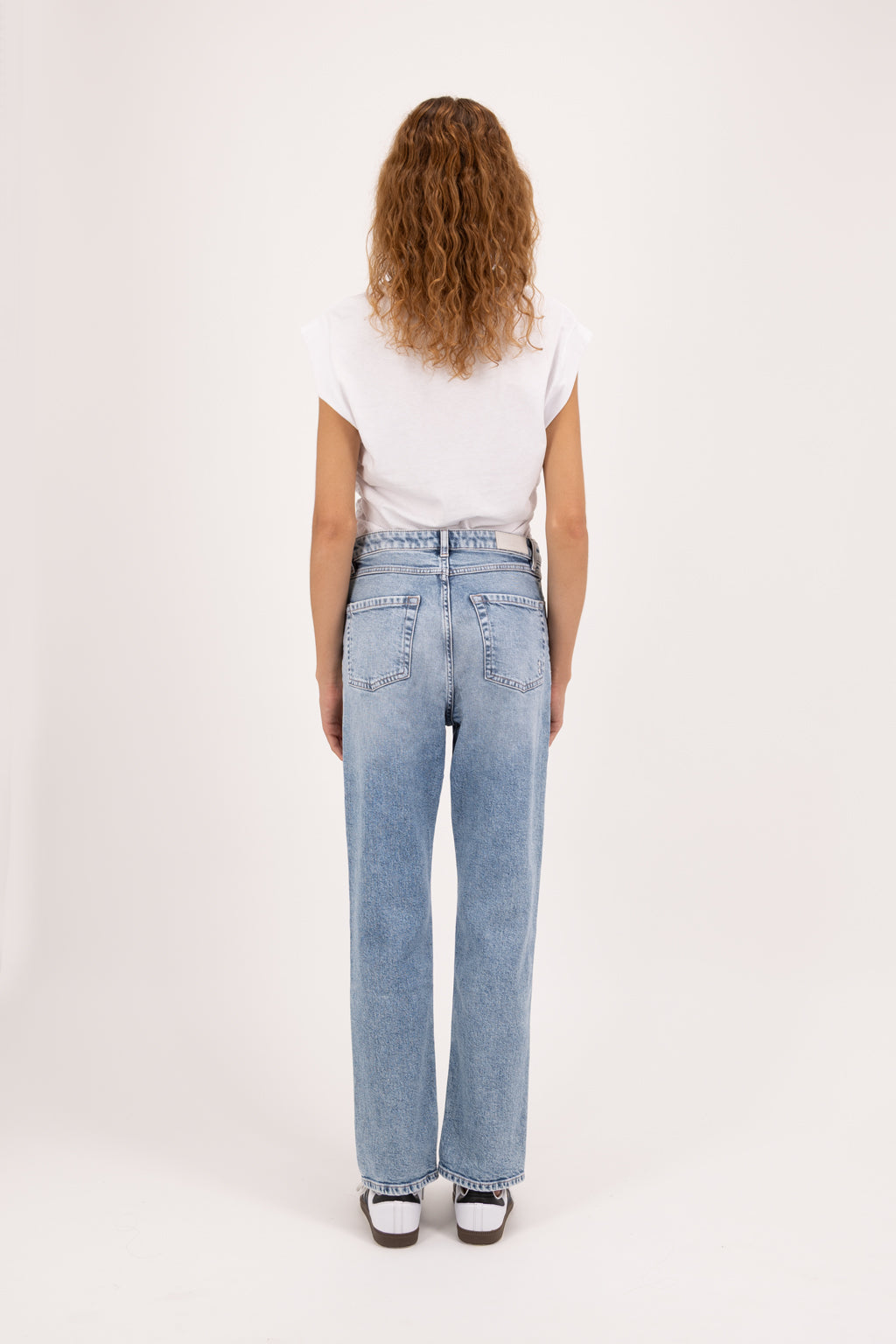 Back view of Roxy women’s slim flared leg jeans in river wash, 100% rigid cotton denim, worn by a model with a white top.