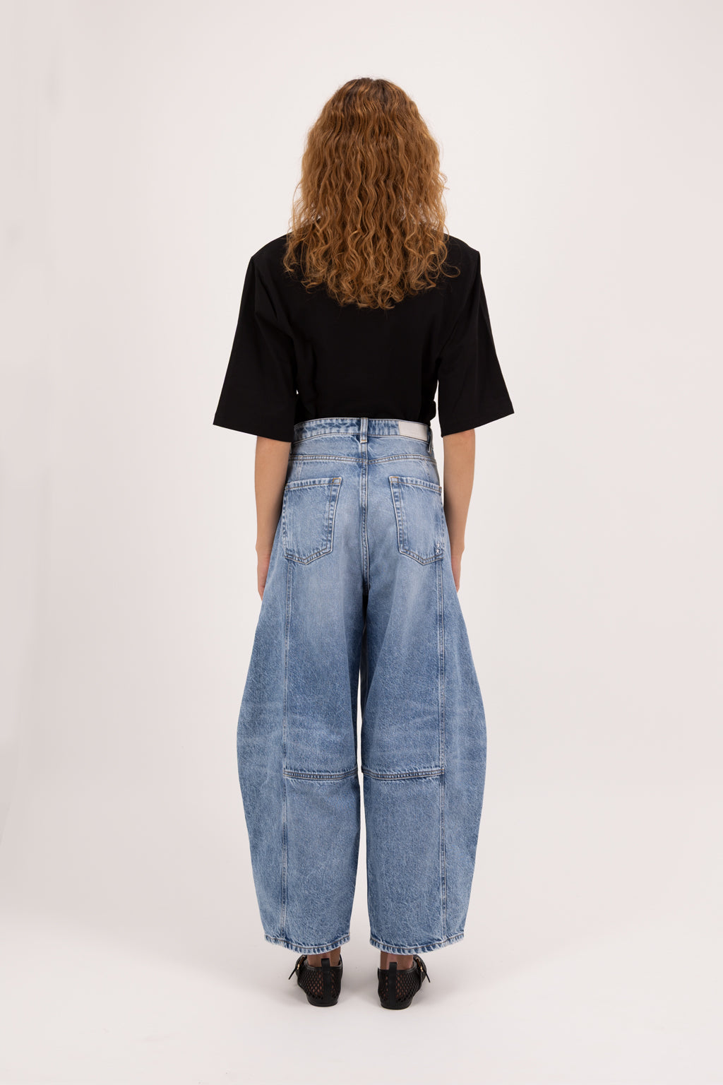 Back view of Sia women’s balloon jeans in river wash, 100% rigid cotton denim, worn by a model with a black t-shirt.
