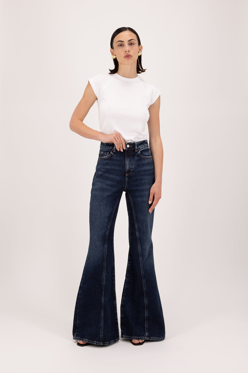 Stella women’s flared leg jeans in deep blue wash, 100% rigid cotton denim, worn by a model with a white top.