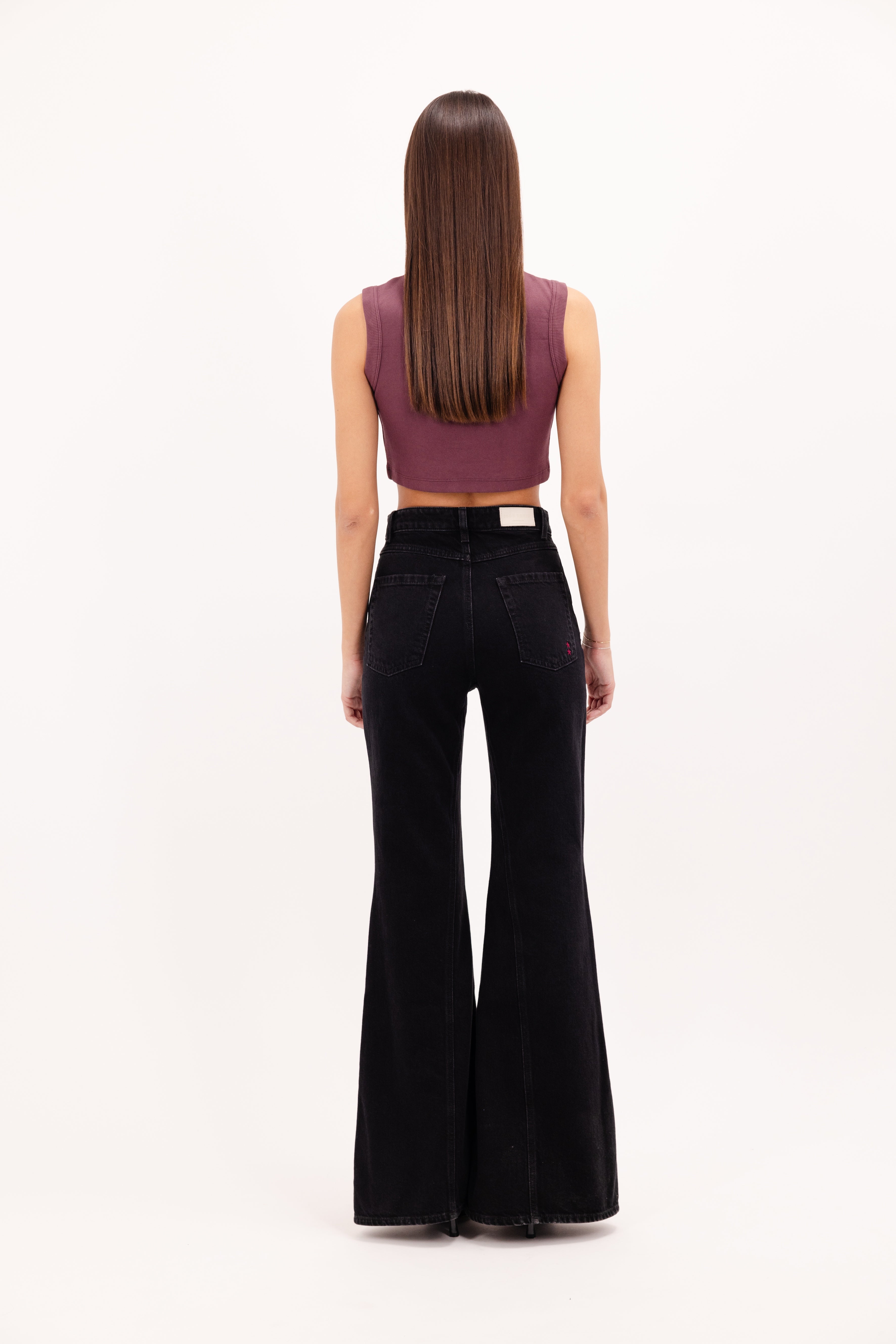 Back view of Stella women’s flared leg jeans in graphite black wash, 100% rigid cotton denim, worn by a model with a cherry top.