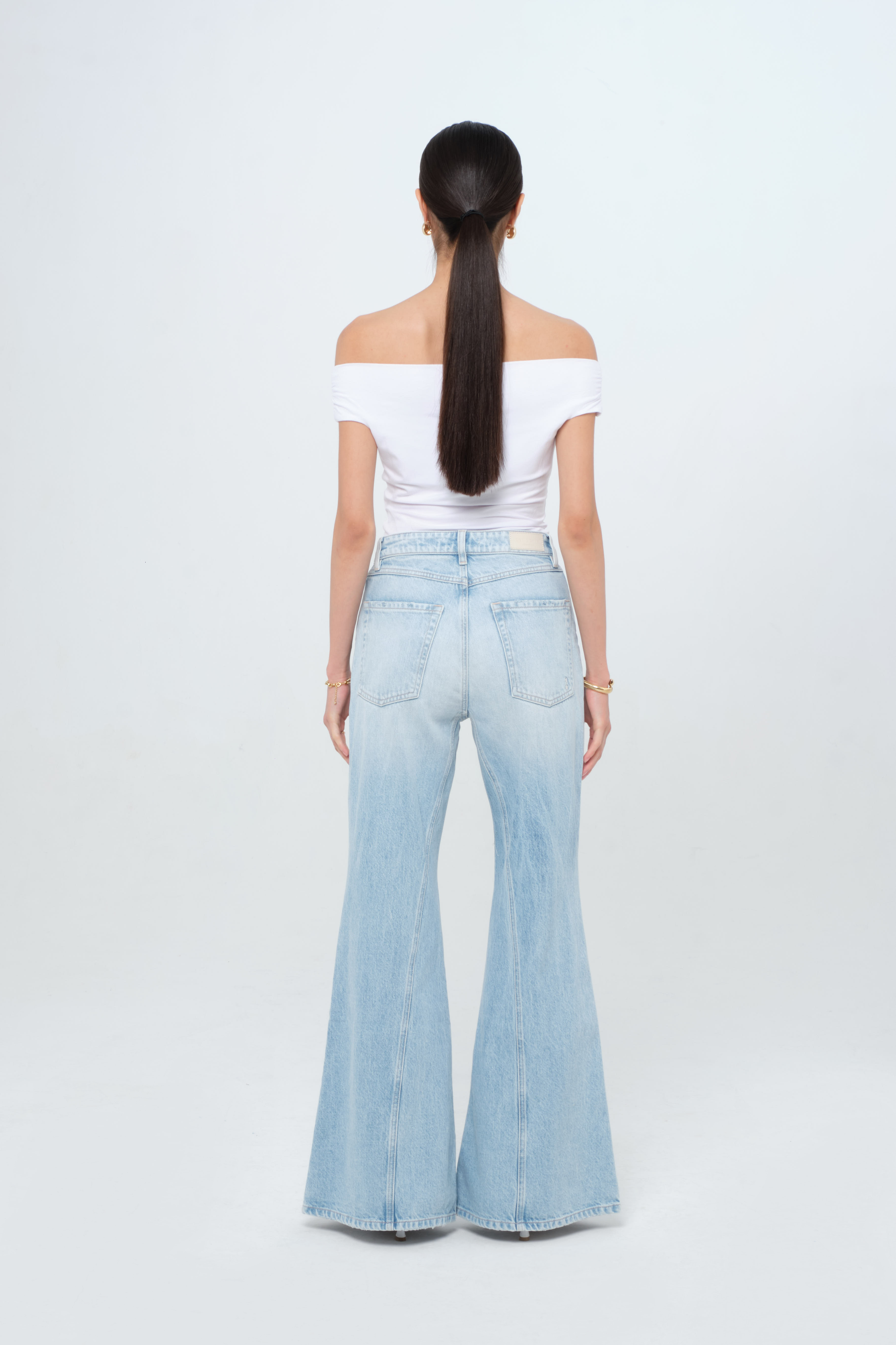 Back view of Stella women’s flared leg jeans in light wash, 100% rigid cotton denim, worn by a model with a white top.