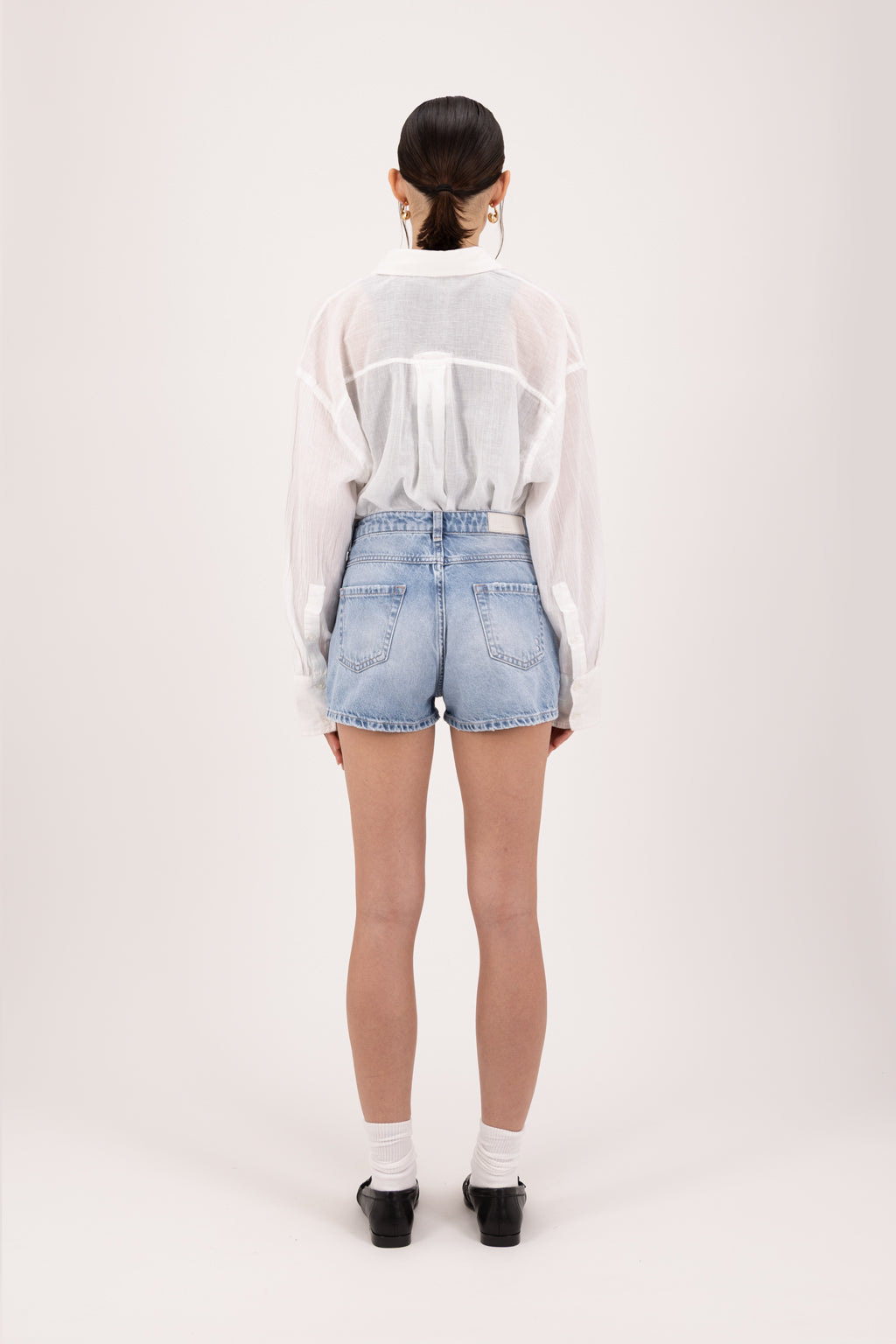 Back view of Tam women’s regular short jeans in sky blue wash, 100% rigid cotton denim, worn by a model with a white shirt. 