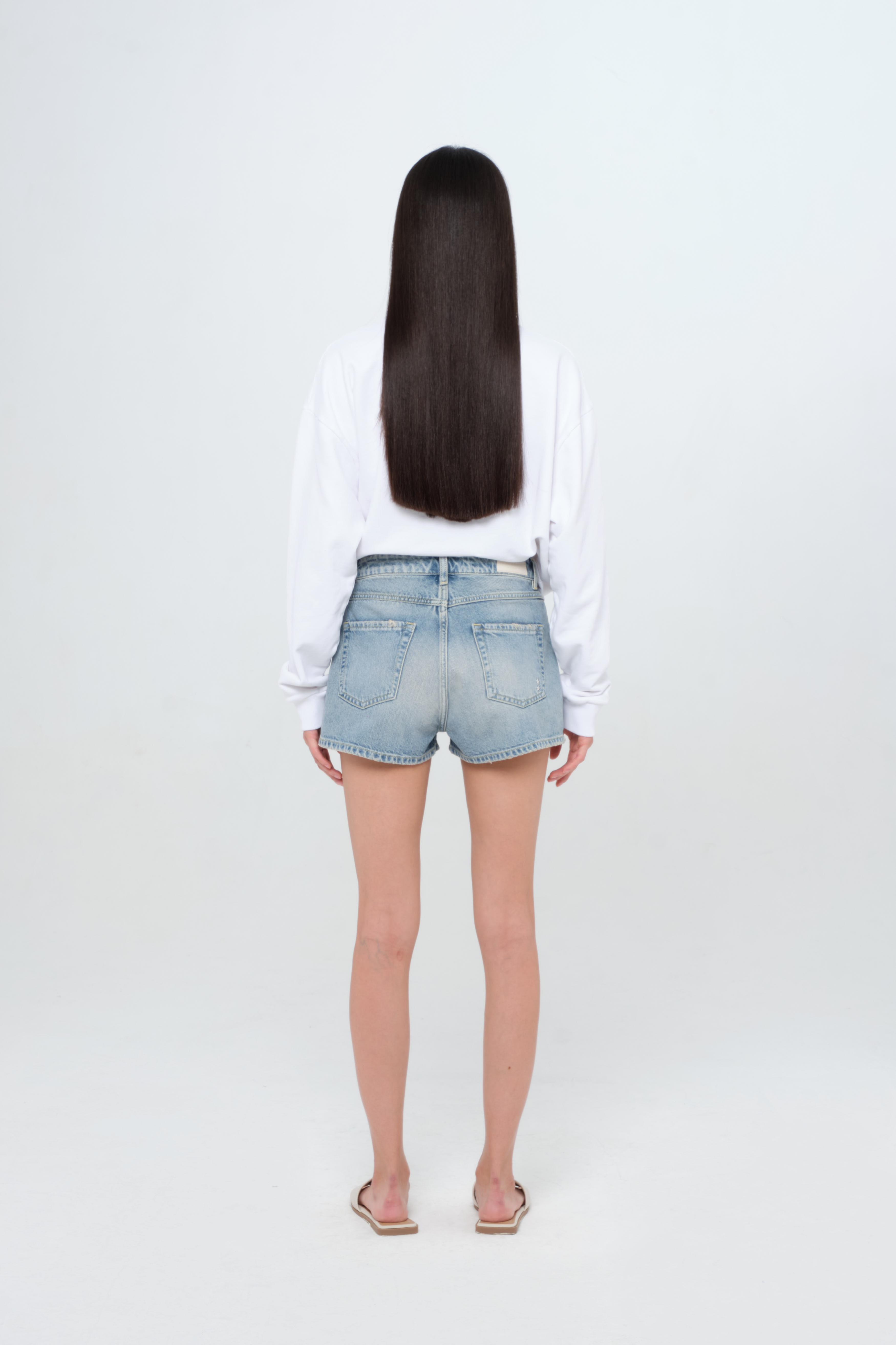 Back view of Tam women’s straight leg jeans in smoke blue wash, 100% rigid cotton denim, worn by a model with a white sweatshirt.
