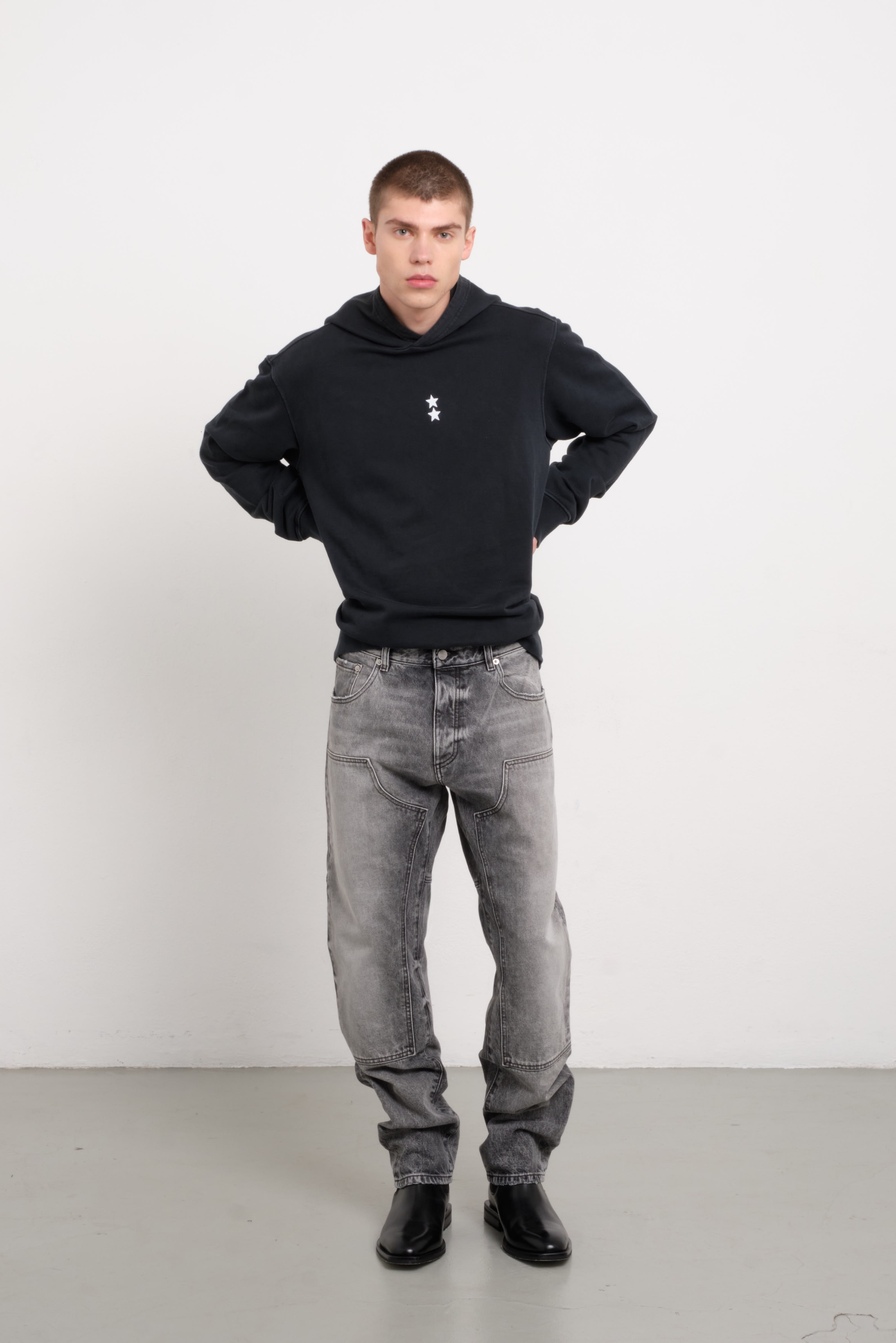 Tavi men’s loose jeans in dark gray wash, 100% rigid cotton denim, worn by a model with a black hoodie.