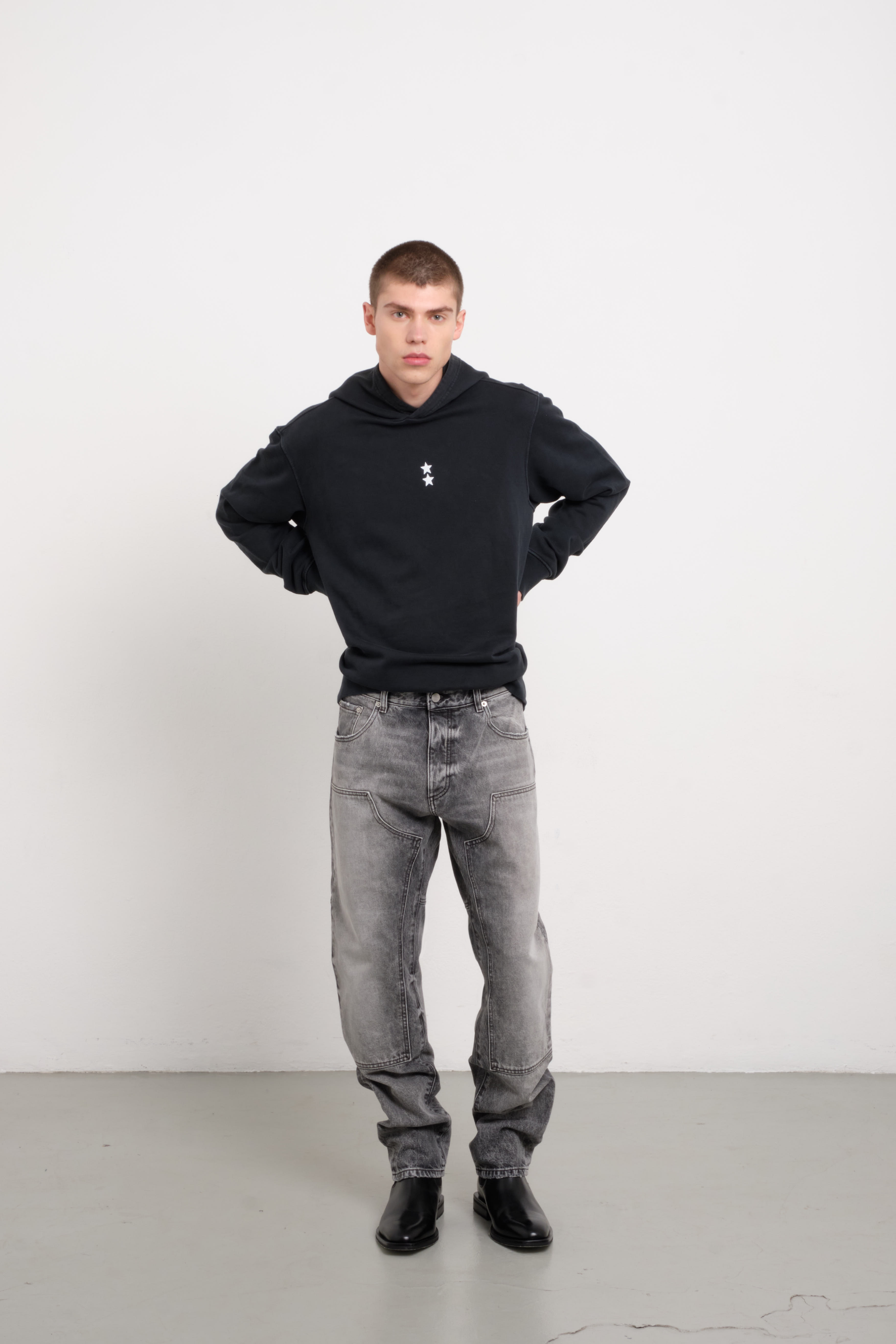 Tavi men’s loose jeans in dark gray wash, 100% rigid cotton denim, worn by a model with a black hoodie.