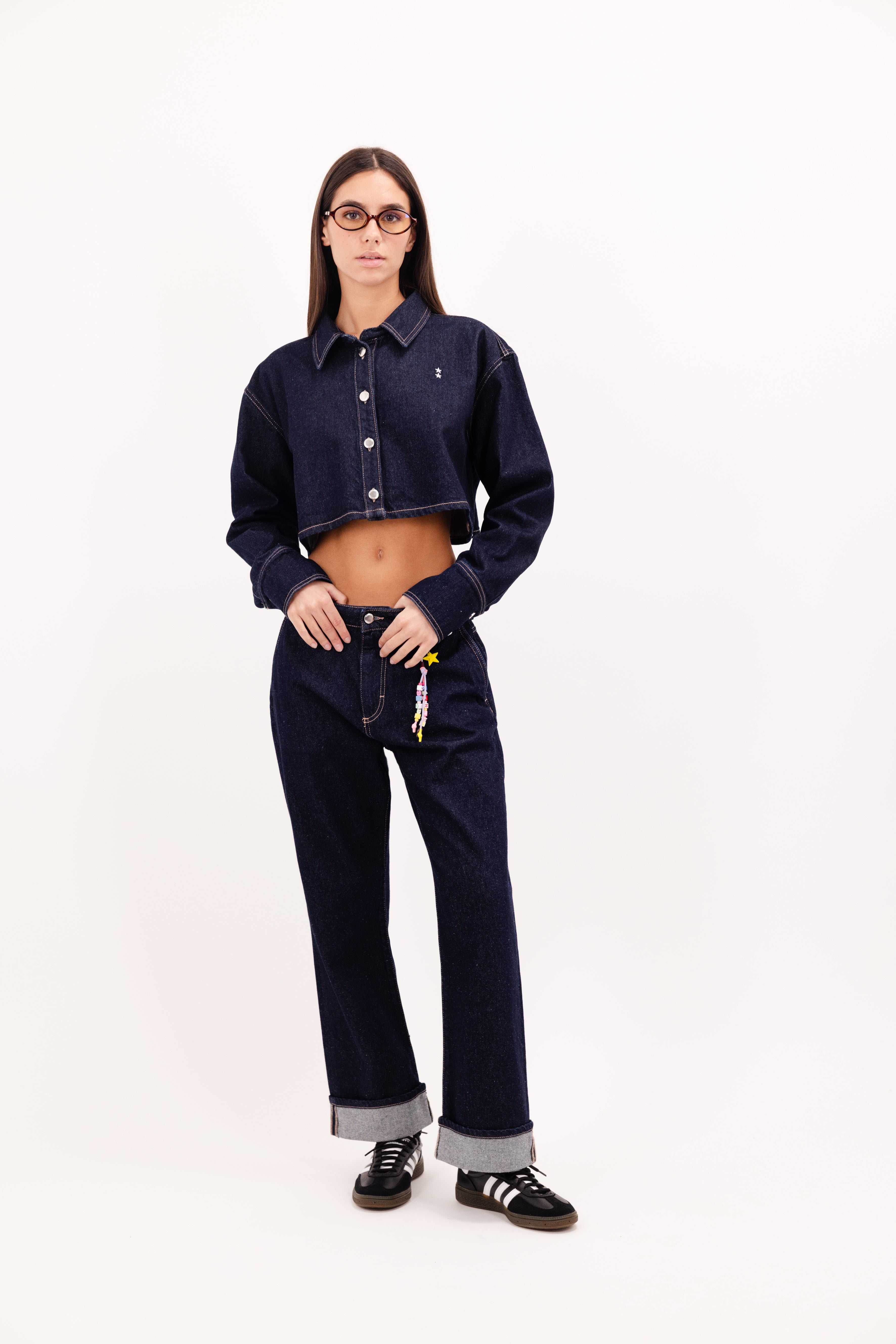 Tiny women’s flared leg jeans in indigo raw, 100% rigid cotton denim, worn by a model with a denim crop shirt.