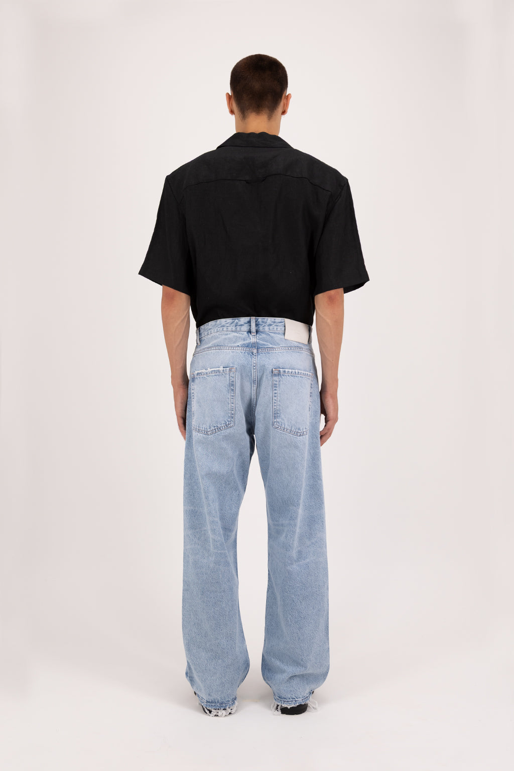 Back view of Will Eco men’s wide leg jeans in arid blue wash, 100% organic rigid cotton denim, worn by a model with a black shirt.