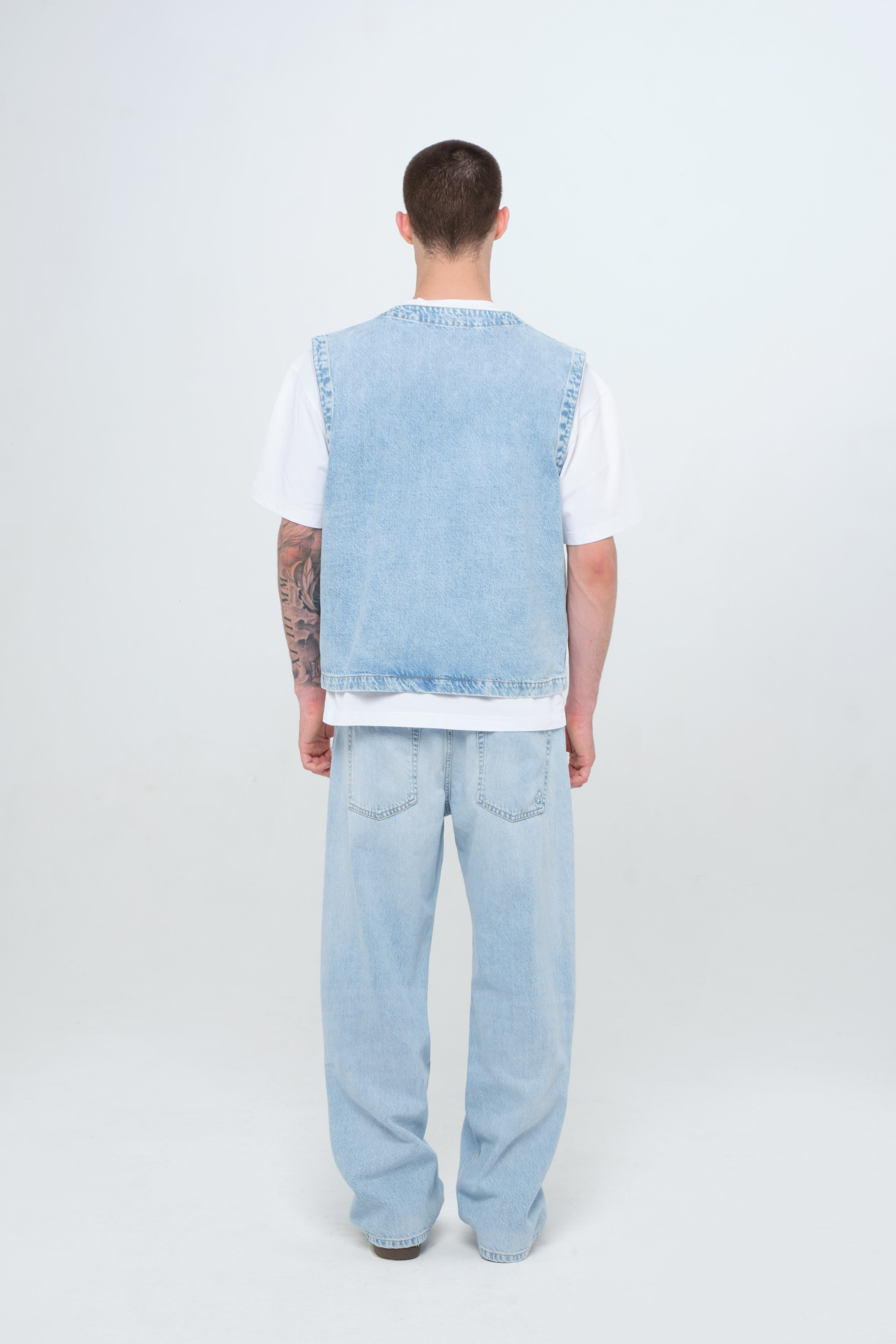 Back view of Will men’s wide leg jeans in light wash, 100% rigid cotton denim, worn by a model with a denim vest.