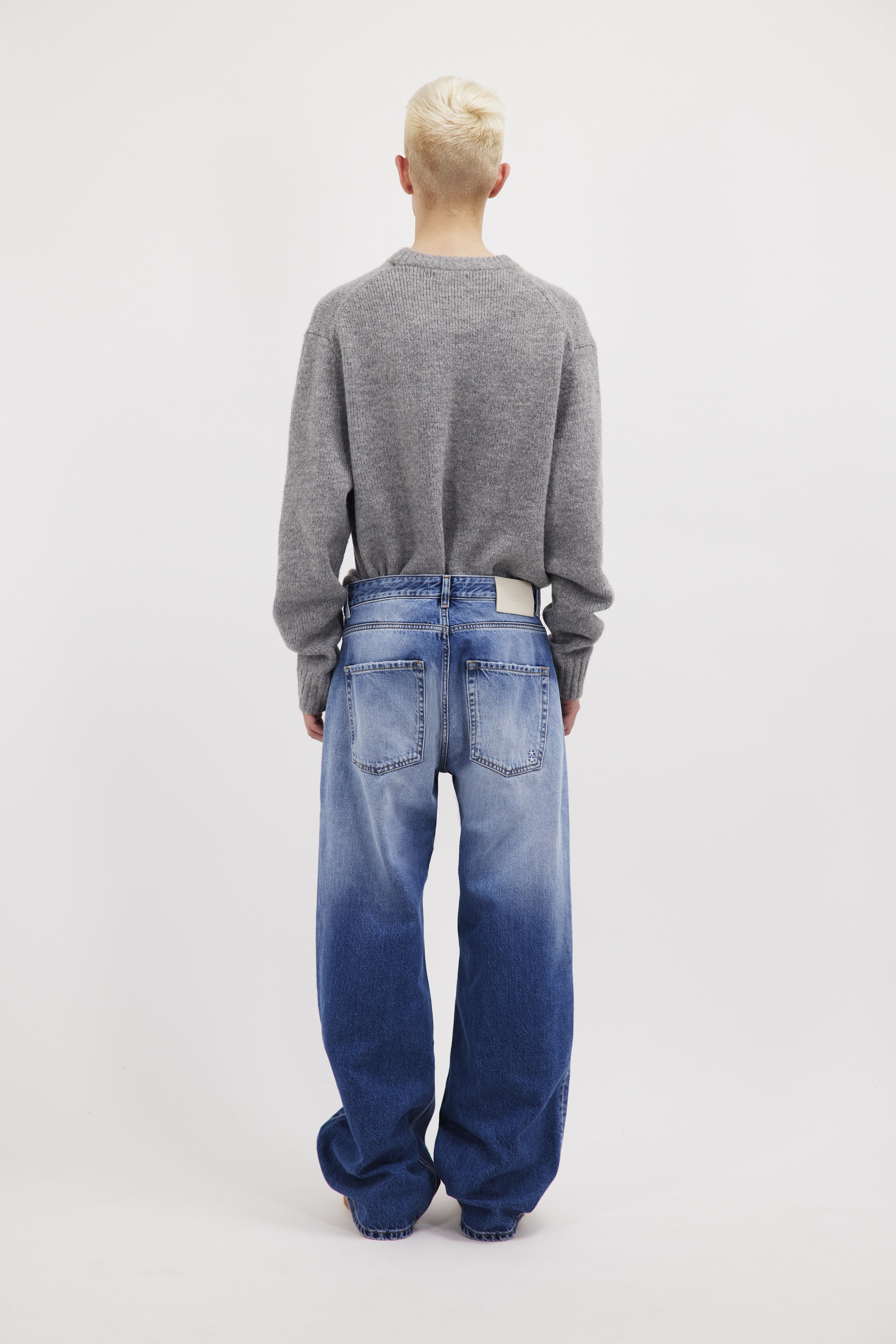 Back view of Will men’s wide leg jeans in misty blue wash, 100% rigid cotton denim, worn by a model with a grey knit.